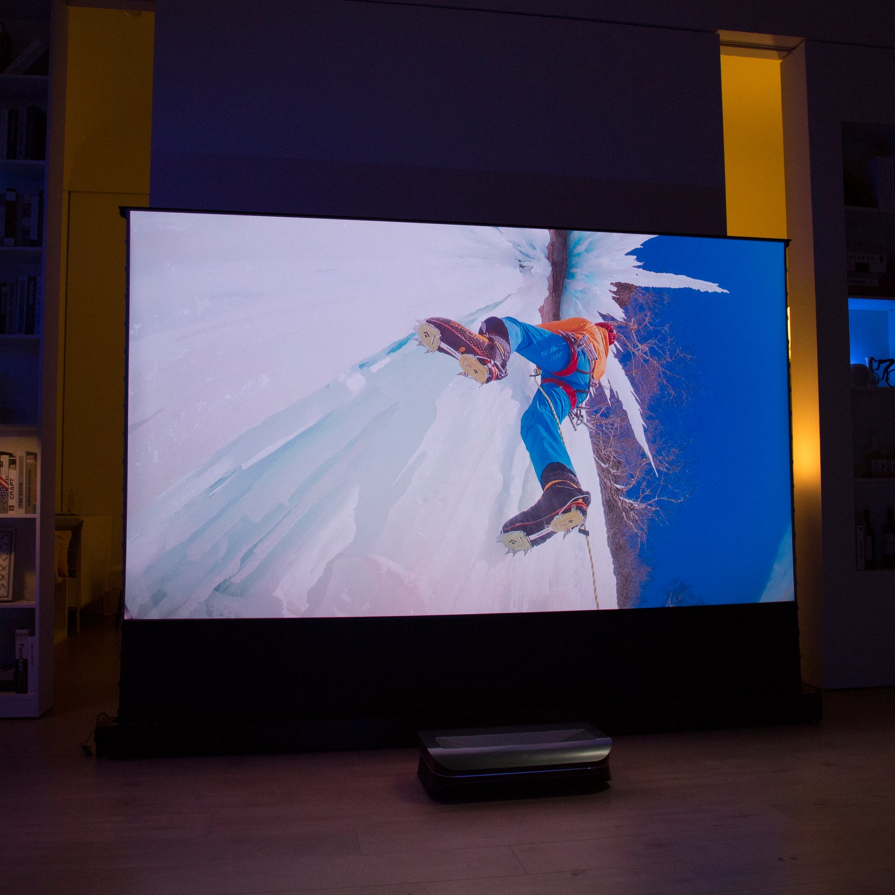 Ice climber ascending a steep slope displayed on a wide AWOL Vision projector screen in a modern living room setting.